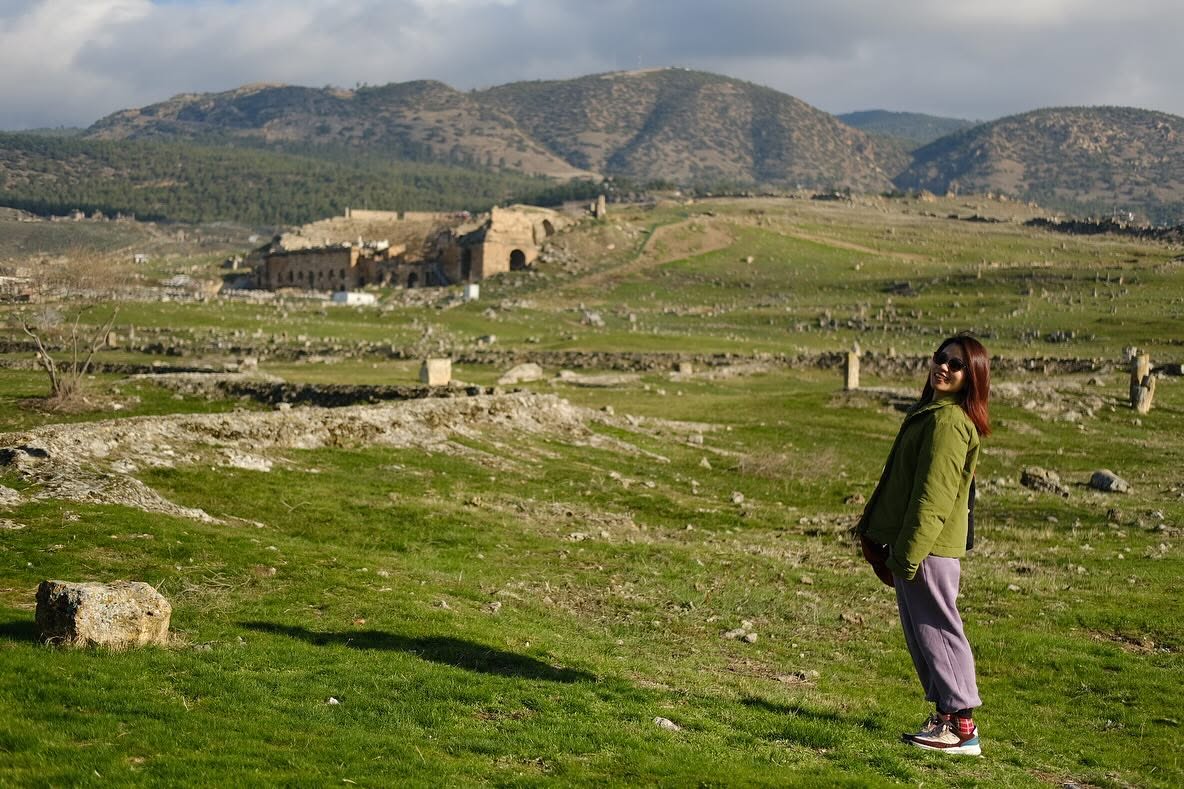 Uyen, founder and editor of AI for Kind, standing on a green hillside with old stone ruins and hills behind her