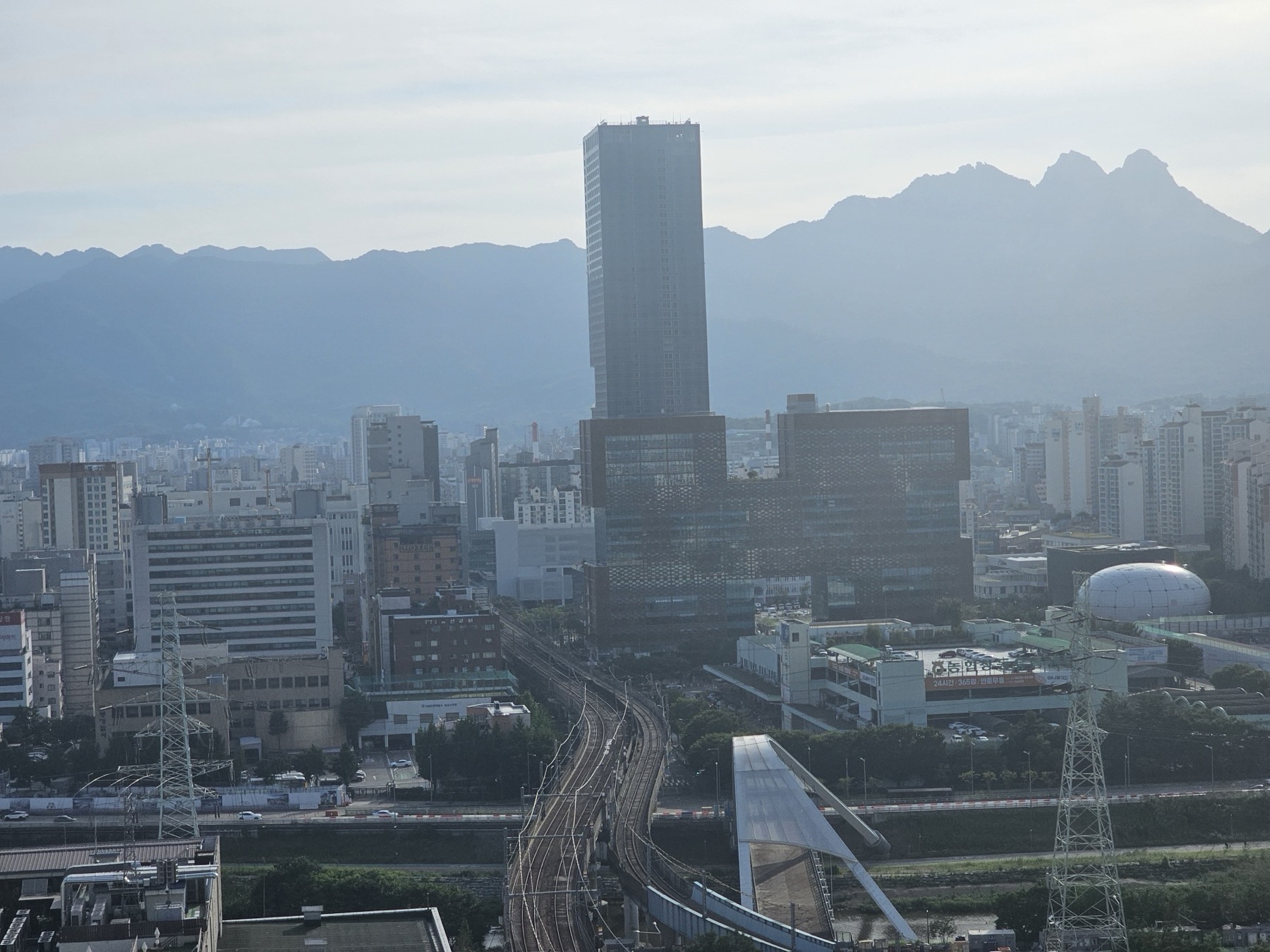 A city view of Chang-dong in Seoul: a tall glass tower above office and apartment blocks, railway tracks in front and mountains behind.