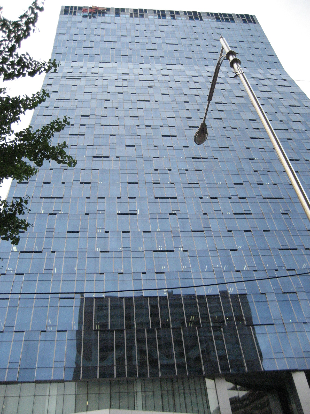 Looking up at a tall glass office tower with the SK logo at the top, a street lamp and tree branches in front.
